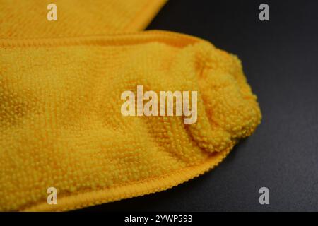 An unusual cleaning cloth, a long yellow microfiber set on a black, matte plastic background. Stock Photo