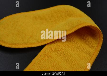 An unusual cleaning cloth, a long yellow microfiber set on a black, matte plastic background. Stock Photo