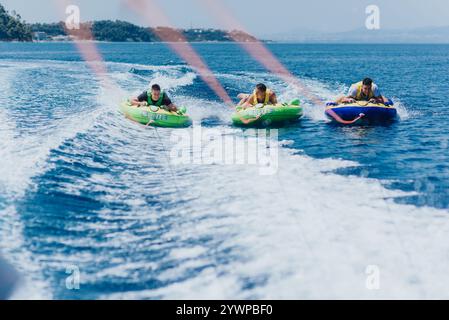 Group of friends enjoying speedboat tubing on the open sea on a sunny day Stock Photo