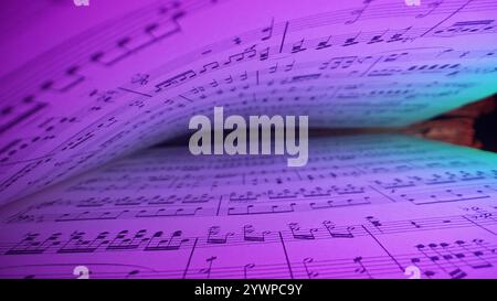 Macro background of saved medieval book with ancient musical notes writings, Glowing Neon Light. Texture of old handwritten classical symphony Stock Photo