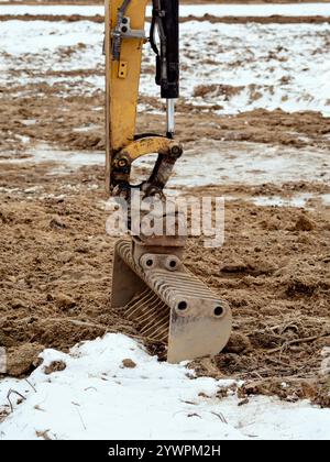 Close-up of an excavator arm digging dirt at a snowy construction site. Industrial work and equipment in winter conditions. Stock Photo