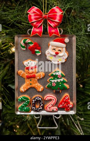Christmas orament cookie tray with bow, candy cane, santa,  gingerbread man, and date on green pine tree background Stock Photo