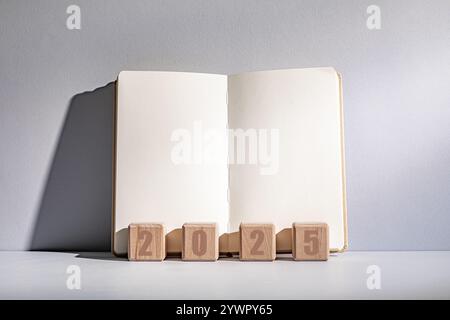 Blank notebook open with wooden blocks spelling out the year 2025 on a simple grey background Stock Photo