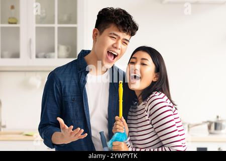 Funny asian couple singing songs while cleaning kitchen Stock Photo