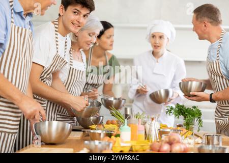 Female chef giving instructions to students standing around table in cooking class Stock Photo
