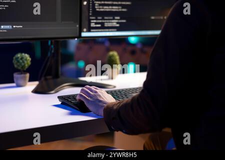 Freelancing programmer doing software debugging on computer at home, checking flaws in lines of code displayed on monitors. IT admin in apartment fixing coding issues, typing on keyboard, close up Stock Photo