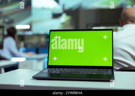 Laptop showing blank greenscreen display in a control center agency, people working with surveillance CCTV cameras to follow the delivery trucks around town. Global positioning system. Stock Photo