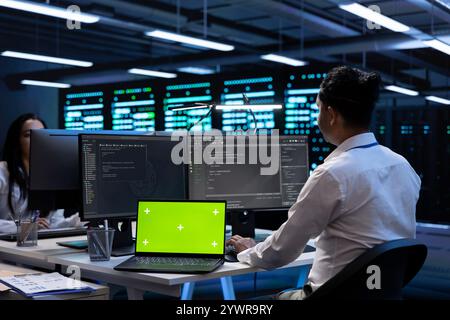 Teamworking programmers in data center using isolated screen laptop to find firewall misconfigurations affecting servers. Workers in server room checking systems bottlenecks using mockup notebook Stock Photo