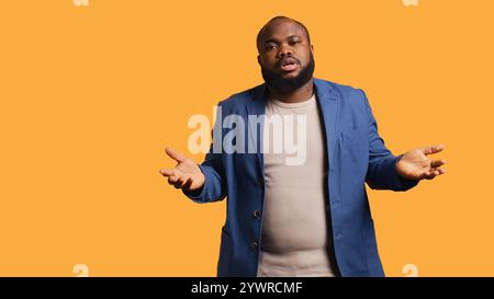 Uncaring man shrugs shoulders, showing indifference and apathy while talking with friend. Careless person doing nonchalant indifferent hand gesturing during conversation, studio background, camera B Stock Photo