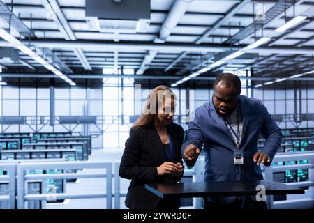 Engineers looking at AR visualization, doing disaster recovery planning in data center. Coworkers using augmented reality in server room to reduce downtime, ensuring business continuity Stock Photo