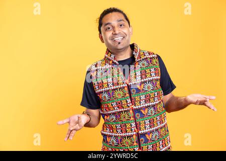 Portrait of cheerful man feeling amused by his lack of knowledge, shrugging shoulders. Jolly person doing questioning hand gesture, feeling entertained by indetermination, studio backdrop Stock Photo