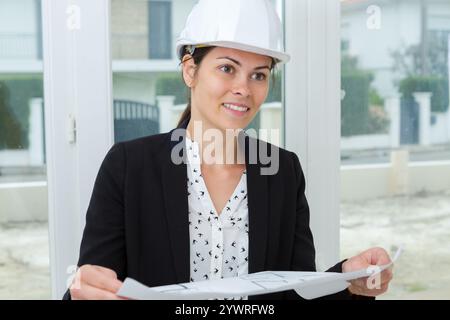young female construction specialist reviewing blueprints at construction site Stock Photo