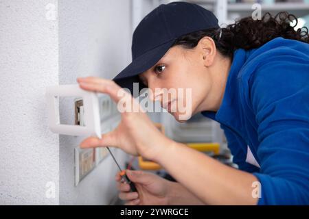 smiling female electrician installing a wall socket Stock Photo
