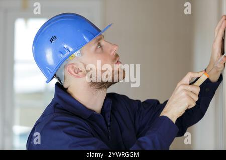 young male builder using scraper on wall Stock Photo