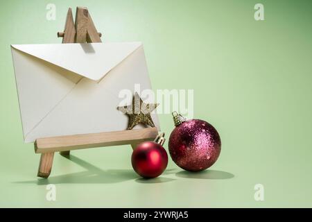 Closeup view of Christmas balls and a star with an envelope on a wooden easel with a colored background. Mockup, blank template, copy space. Greeting Stock Photo