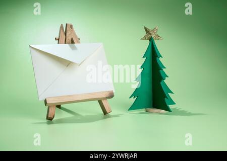 Closeup view of a Christmas tree miniature and star with an envelope on a wooden easel with a colored background. Mockup, blank template, copy space. Stock Photo