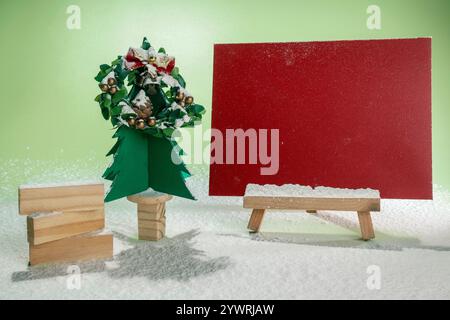 Christmas tree miniature and Christmas wreath with wooden block stack and envelope on wooden easel with snow on colored background. Mockup, blank temp Stock Photo