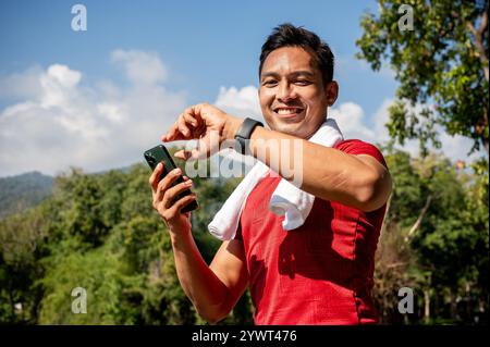 A healthy, happy Asian man in sportswear checks his calorie count on his smartwatch while jogging in a park on a hot, summer day. people, lifestyles, Stock Photo