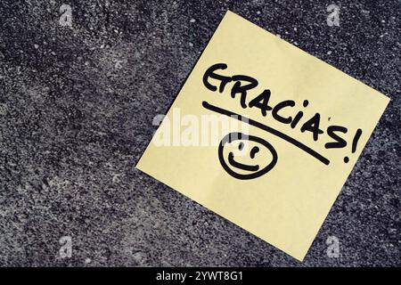 Thank you in spanish written on a post-it or note on table. Stock Photo