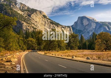 Road in Yosemite National Park, California, leading toward Half Dome rock formation in autumn; blue sky with clouds in background Stock Photo