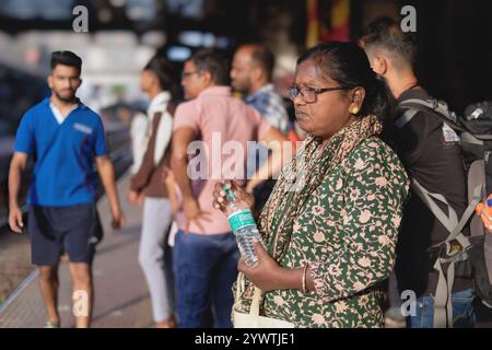 An Indian woman waiting on a railway platform at Dadar Station, Mumbai, India, clutching a bottle of water, with male passengers in the background Stock Photo