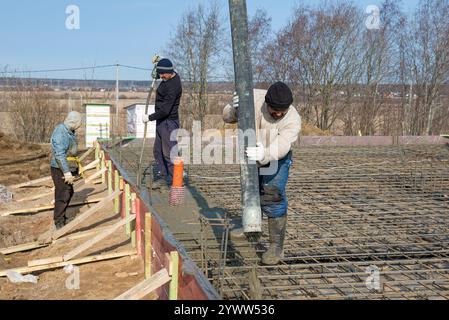 LENINGRAD REGION, RUSSIA - MARCH 28, 2021: Migrant construction workers pour the foundation of a country house on a sunny March day Stock Photo