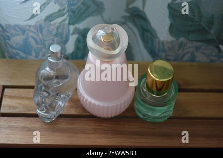 Three glass bottles. One clear skull-shaped glass, an exquisite pink glass bottle and a bottle of green liquid perfume are set on a wooden background. Stock Photo