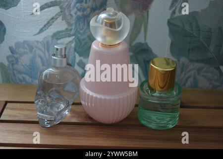 Three glass bottles. One clear skull-shaped glass, an exquisite pink glass bottle and a bottle of green liquid perfume are set on a wooden background. Stock Photo