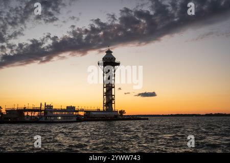 The silhouetted Bicentennial Tower and pier stand under a band of dark clouds over a glowing orange horizon and choppy water in Erie, Pennsylvania. Stock Photo