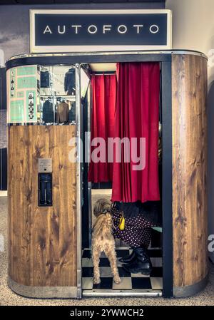 Photo booth exterior with red curtain partially drawn, revealing a woman and her dog inside Stock Photo