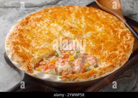 Tasty creamy salmon vegetables pot pie with crispy puff crust closeup on the baking dish on the table. Horizontal Stock Photo