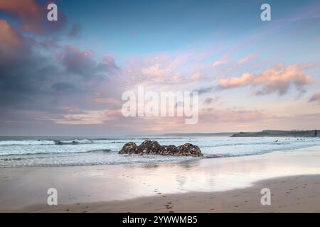 Pastel coloured sky over rocks exposed by a low tide on Gt Western Beach on the coast of Newquay in Cornwall in the UK. Stock Photo