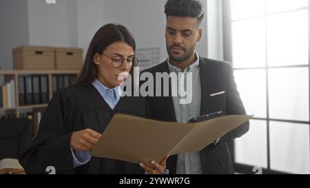 Man and woman in a workplace, with the woman wearing a judge's robe, attentively reviewing documents together indoors. Stock Photo