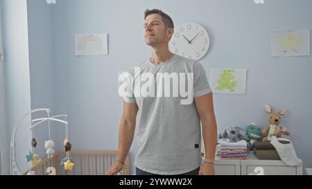 Handsome man standing in a baby room with stuffed animals and colorful drawings, surrounded by a cradle and decorations, creating a warm and inviting Stock Photo