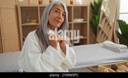 Elderly woman enjoying a spa treatment in a serene wellness center, wearing a white robe with grey hair, posing confidently indoors Stock Photo