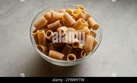 Bowl of dry rigatoni pasta on a gray countertop in natural light emphasizing its texture and color Stock Photo