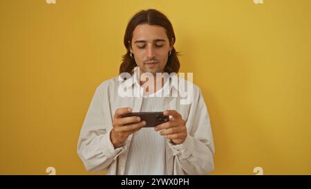 Young hispanic man with long hair using smartphone over isolated yellow background Stock Photo