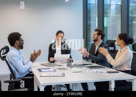 A group of business professionals in a modern office celebrating a shared achievement with smiles and applause, enhancing teamwork and support within a collaborative environment. Stock Photo