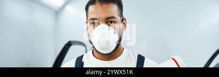A skilled mechanic wearing a mask and work attire prepares for a task in a busy garage. Stock Photo