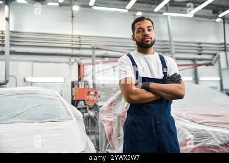 Handsome mechanic stands strong with arms crossed, ready for work in a busy automotive shop Stock Photo