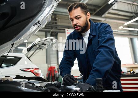 Handsome mechanic focused on repairing a car engine in a well equipped garage. Stock Photo