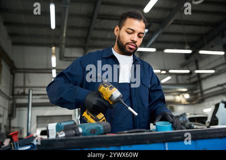 Handsome young mechanic uses a power drill while focusing on a task in a busy workshop. Stock Photo