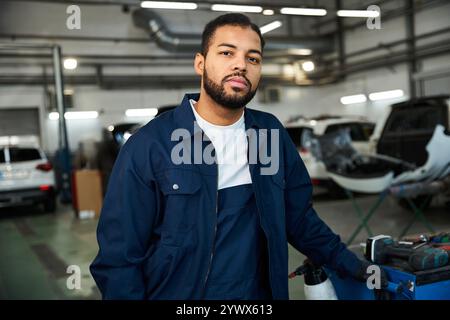 Handsome young mechanic stands confidently while working in a bright and busy garage area Stock Photo