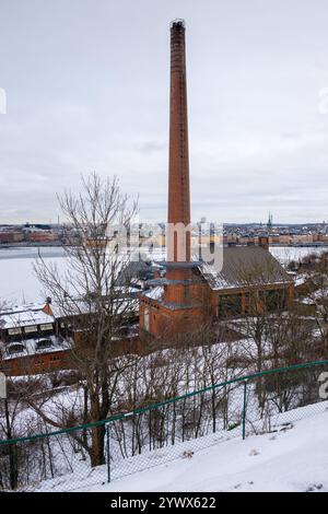 A winter view of an old brick building with a tall chimney, surrounded by snow and trees. This scene captures the essence of Stockholm's chilly water Stock Photo