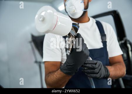 Skilled mechanic focuses intently while using a spray gun for auto body work in a garage. Stock Photo