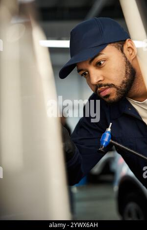 A dedicated young mechanic intently fixes a vehicle in a tool filled repair shop. Stock Photo