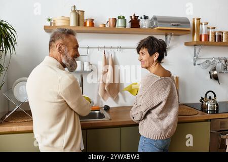 A happy senior couple enjoys washing dishes together in their cozy kitchen. Stock Photo