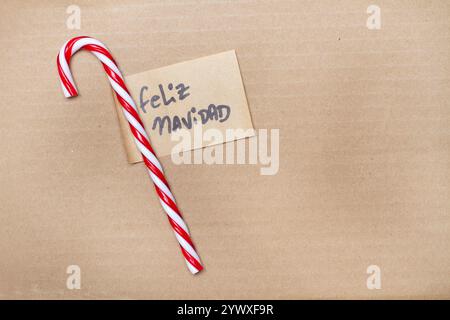 Red and white striped candy cane with a feliz navidad message on a brown background with copy space (trad. merry christmas) Stock Photo