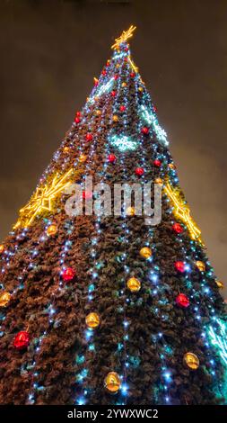 Big Christmas tree decorated with large glowing snowflakes, garlands and colorful balls against the night sky, view from below Stock Photo