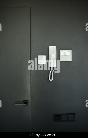 Vertical shot of intercom electronic panel and handset with microphone for talking to guests hanging on black wall inside minimalist apartment in residential building, copy space Stock Photo